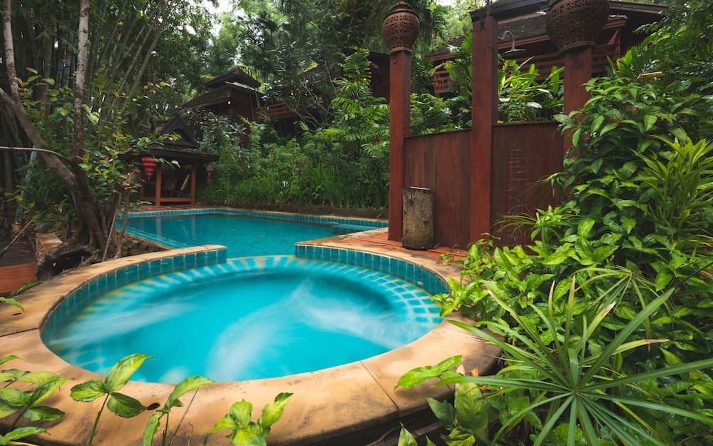 A serene tropical resort pool surrounded by lush greenery and wooden structures offers a tranquil escape for travelers seeking relaxation in nature.