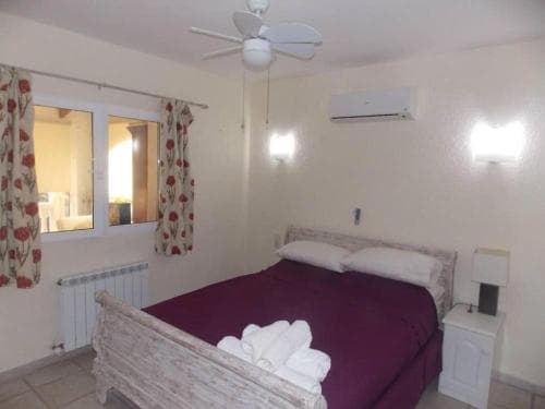 A cozy hotel room features a neatly made bed with purple bedding, floral curtains, and a ceiling fan, ideal for travelers seeking comfort and relaxation.