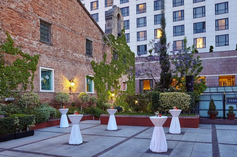 A serene courtyard at the InterContinental Buenos Aires by IHG features ivy-covered brick walls, elegant white cocktail tables, lush greenery, and a backdrop of modern hotel windows, ideal for intimate gatherings or romantic evenings.
