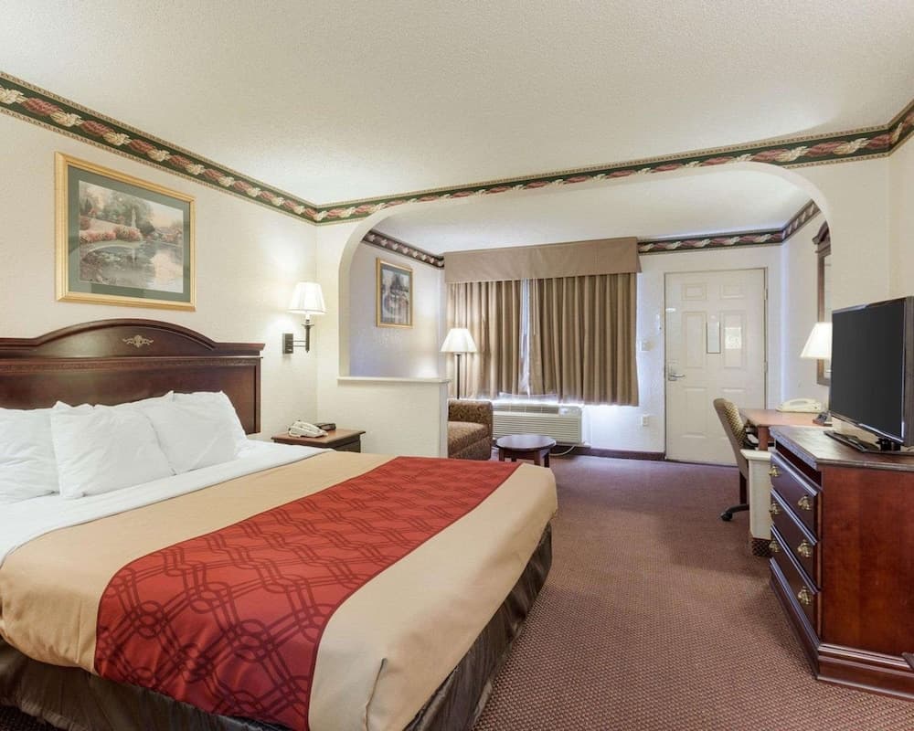 A cozy hotel room features a neatly made bed with red accents, warm lighting, and a functional desk area, ideal for travelers seeking comfort and convenience during their stay.