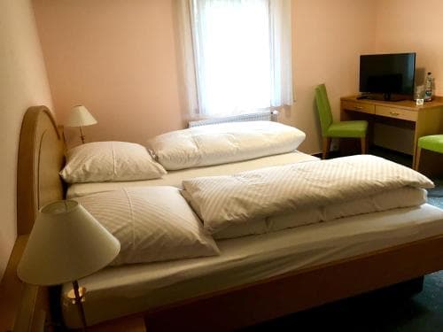 A cozy hotel room features a neatly made bed with white linens, a desk with a TV, and soft lighting, creating a serene atmosphere ideal for travelers seeking rest and relaxation.