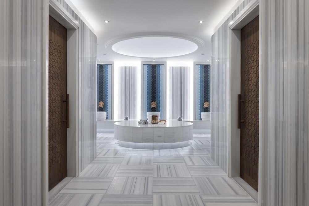 A serene spa hallway features elegant marble flooring, modern wooden doors, and a central circular table under soft lighting, ideal for relaxation and wellness retreats.