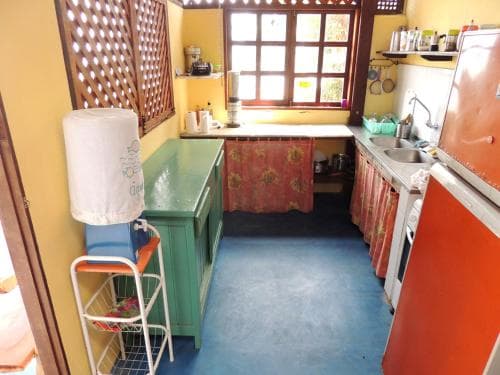 A cozy kitchen with vibrant orange and green cabinets, a blue floor, and a window with a lattice frame invites travelers seeking a warm, homey atmosphere for culinary adventures.