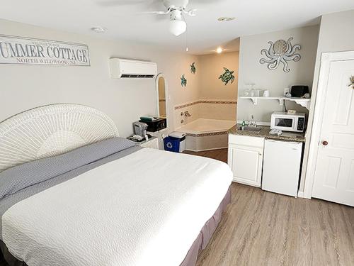 A cozy beachside cottage bedroom features a neatly made bed, a small kitchenette with a microwave, and a bathtub, creating a serene and inviting atmosphere ideal for a relaxing seaside getaway.