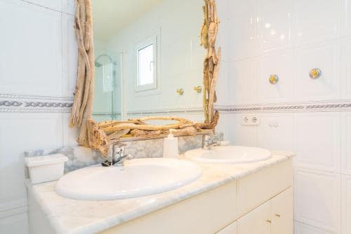 A serene coastal-themed bathroom features dual sinks under a driftwood-framed mirror, ideal for travelers seeking a relaxing seaside retreat ambiance.