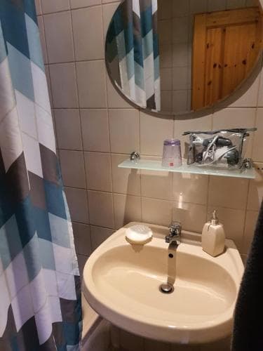 A cozy bathroom with tiled walls, a round mirror, and a patterned shower curtain creates a serene atmosphere, ideal for travelers seeking comfort in compact accommodations.