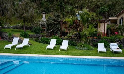 A serene tropical resort features a vibrant blue pool surrounded by lush greenery, white lounge chairs, and a cozy villa, ideal for relaxing vacations.