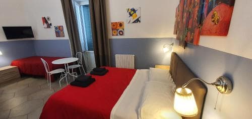 A cozy hotel room with vibrant wall art, red bedding, and warm lighting creates an inviting atmosphere ideal for travelers seeking comfort and artistic ambiance.