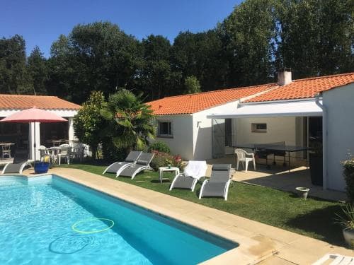 A serene vacation rental features a sparkling pool, lounge chairs, and a cozy patio under a clear blue sky, ideal for family getaways in a tranquil suburban setting.