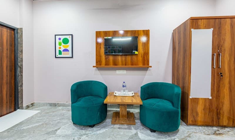 A cozy hotel room in Ayodhya features teal armchairs, a wooden TV console, and modern decor, ideal for travelers seeking comfort and relaxation during their stay.