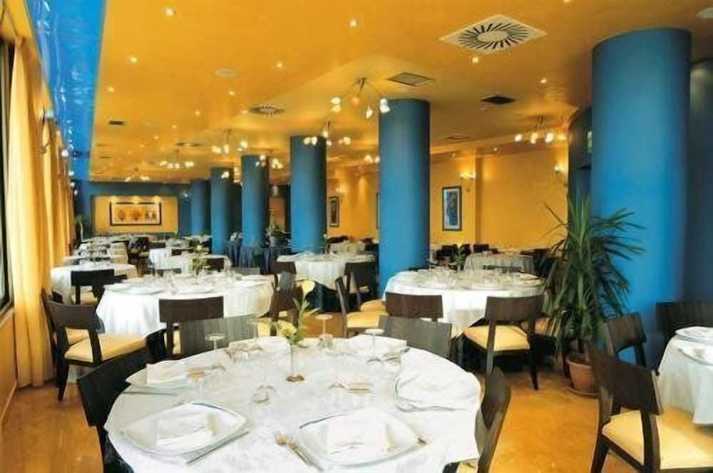 A warmly lit indoor restaurant with blue columns, round tables set for dining, and potted plants creates an inviting atmosphere ideal for travelers seeking a cozy dining experience.