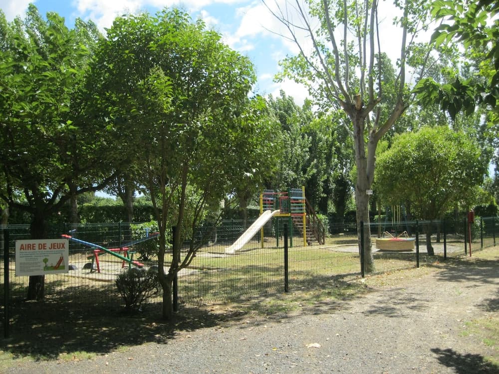 A serene outdoor playground surrounded by lush green trees offers a fun-filled environment with slides, swings, and climbing structures, ideal for family outings and children's activities.