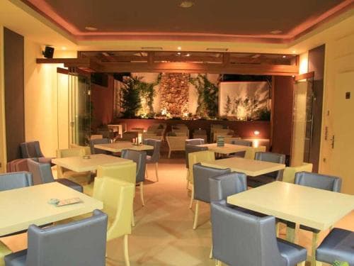 A cozy indoor restaurant features neatly arranged tables with blue chairs, warm lighting, and a lush green wall centerpiece, creating an inviting atmosphere ideal for travelers seeking a comfortable dining experience.