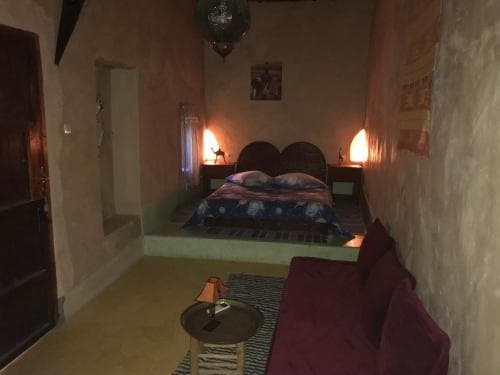 A cozy, warmly lit bedroom with rustic walls, a low bed adorned with patterned bedding, and a plush sofa invites travelers seeking a serene and intimate retreat experience.