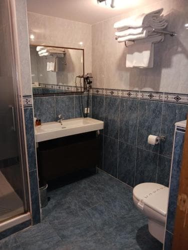 A cozy hotel bathroom with blue tiled walls, a sink, toilet, and neatly folded towels on a rack, ideal for travelers seeking comfort and cleanliness during their stay.