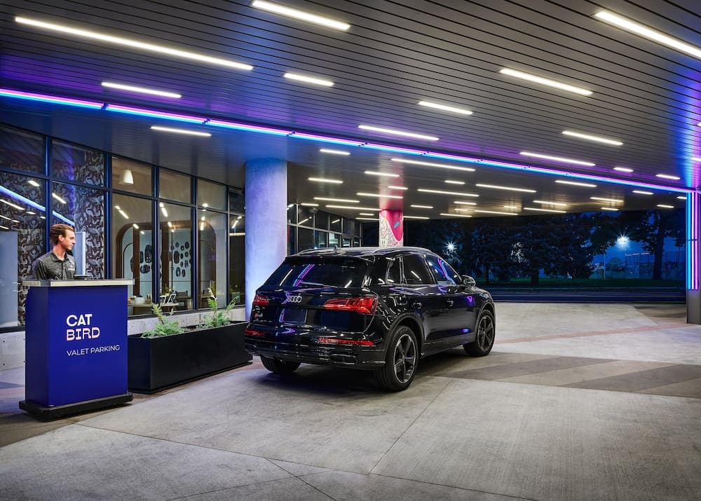 A sleek black SUV is parked under a modern valet parking structure illuminated by vibrant neon lights, creating an upscale urban atmosphere ideal for travelers seeking premium services.
