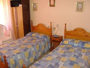 A cozy hotel room features two wooden beds with blue and yellow checkered bedding, framed pictures on the walls, and a small nightstand, ideal for travelers seeking a comfortable and budget-friendly stay.