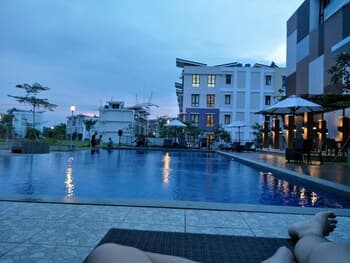 A serene evening at an outdoor hotel poolside area features calm waters reflecting the twilight sky, surrounded by lounge chairs and umbrellas, ideal for travelers seeking relaxation and leisure.