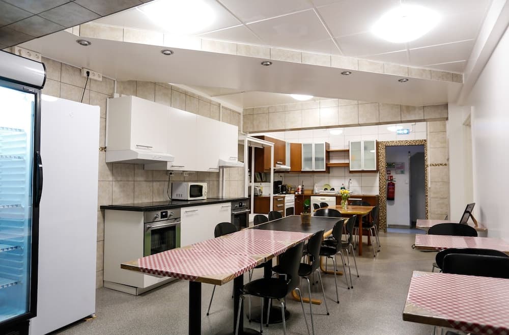 A cozy communal kitchen area with checkered tablecloths, modern appliances, and ample seating offers a welcoming space for travelers seeking a homey dining experience.