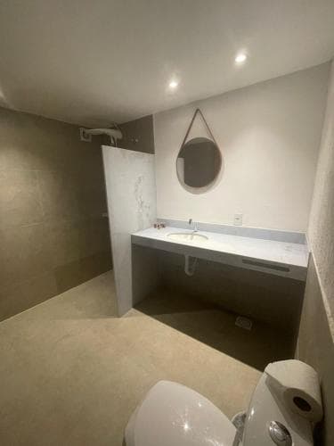 A modern bathroom with sleek white fixtures, a round mirror, and soft lighting creates a serene atmosphere, ideal for travelers seeking a clean and minimalist accommodation space.