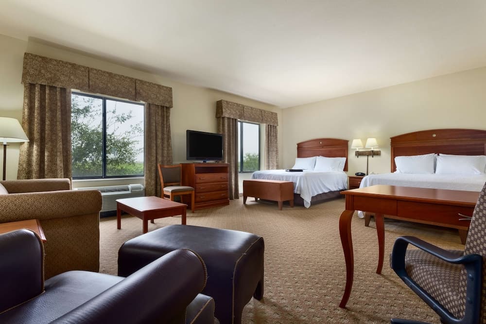 A cozy hotel room with two beds, a sitting area, and large windows offering a serene view of greenery, ideal for travelers seeking comfort and relaxation.