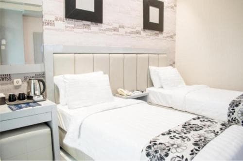 A cozy hotel room features two neatly made beds with white linens, a modern bedside table, and decorative wall art, creating a welcoming atmosphere ideal for travelers seeking comfort and relaxation.