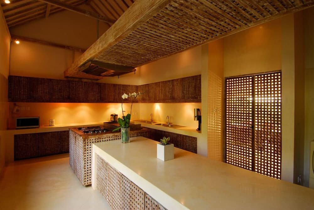 A warmly lit tropical kitchen with woven bamboo accents, a central island, and a lattice door evokes a serene and inviting atmosphere ideal for eco-friendly retreats.
