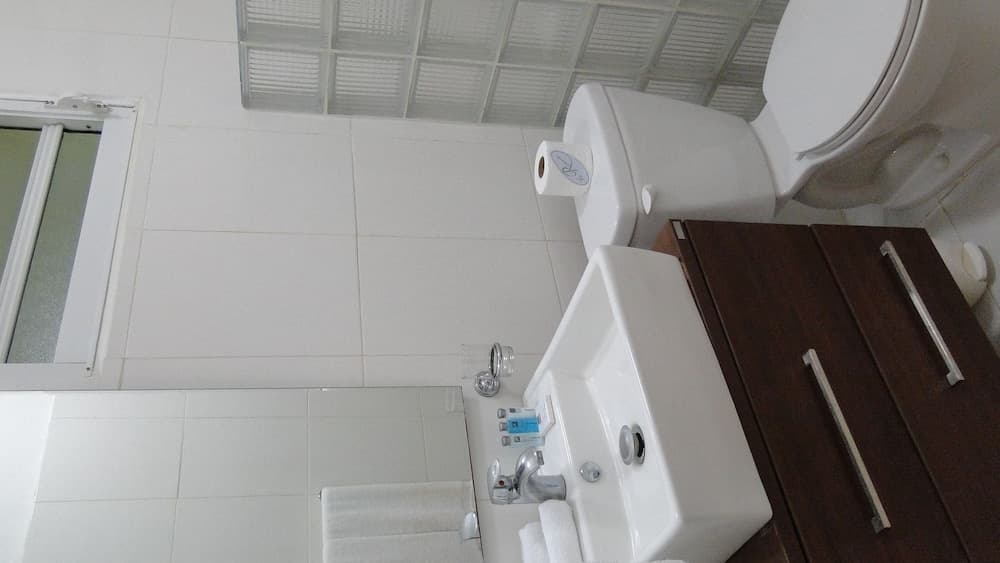 A clean and modern bathroom with white tiles, a glass block window, a wooden cabinet, and neatly arranged toiletries, ideal for travelers seeking comfort and hygiene.