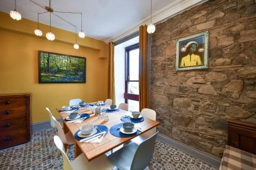 A cozy dining room with a rustic stone wall, warm yellow accents, and modern lighting creates an inviting atmosphere perfect for travelers seeking a charming and intimate meal setting.