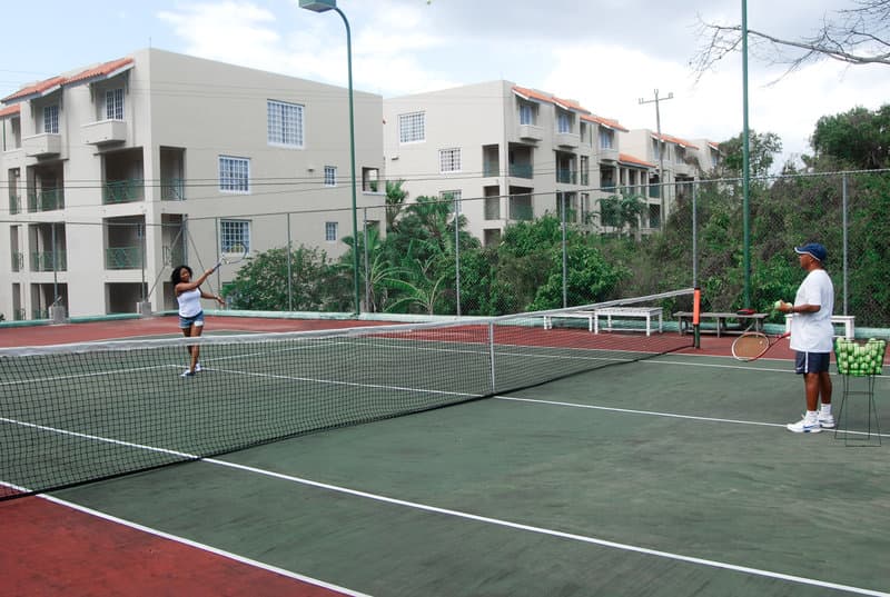 A vibrant tennis court surrounded by lush greenery and apartment buildings sets the stage for an active and engaging outdoor sports session, ideal for travelers seeking recreational activities in a serene residential area.