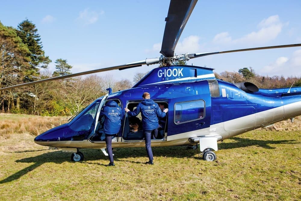 A serene outdoor scene features two individuals boarding a blue helicopter on a grassy field under a clear sky, ideal for adventure seekers exploring unique travel experiences.