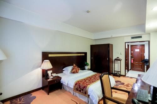 A cozy hotel room features a neatly made bed with decorative pillows, a desk with a computer, warm lighting, and a welcoming ambiance, ideal for travelers seeking comfort and functionality during their stay.
