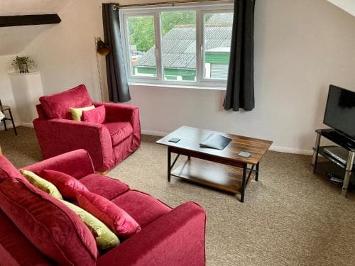 A cozy living room with plush red sofas, a wooden coffee table, and a bright window view of rooftops, ideal for a comfortable stay in a vacation rental.