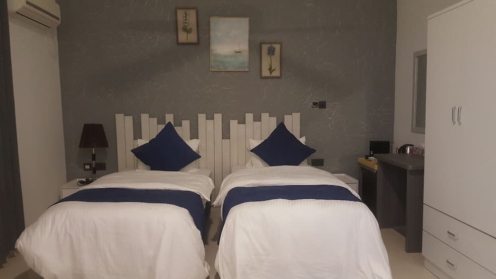 A cozy hotel room features two neatly made beds with blue accents against a gray textured wall adorned with framed artwork, ideal for travelers seeking comfort and simplicity.