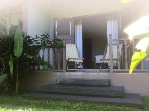 A serene tropical villa porch features wooden chairs, lush greenery, and inviting steps, perfect for a relaxing vacation getaway.