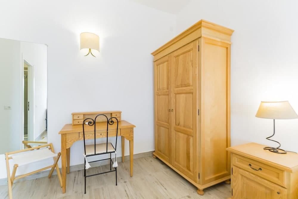 A cozy bedroom features a wooden desk with a black chair, a large wardrobe, and soft lighting, creating a serene atmosphere ideal for travelers seeking comfort and functionality in their accommodations.