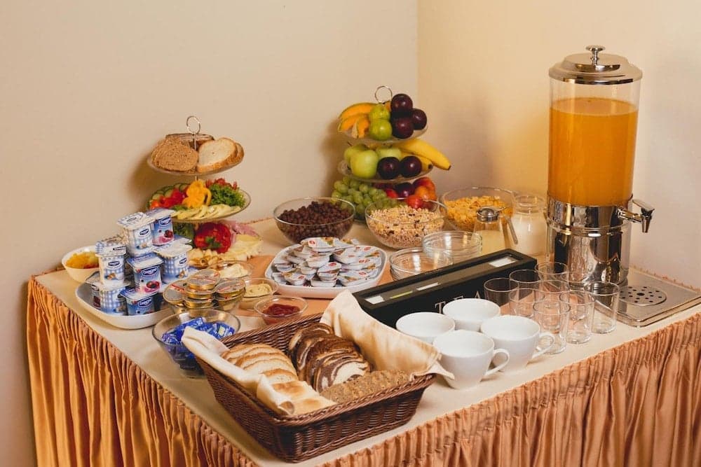 A cozy hotel breakfast buffet table adorned with fresh fruits, assorted breads, yogurt cups, and a juice dispenser invites travelers to start their day with a hearty meal.