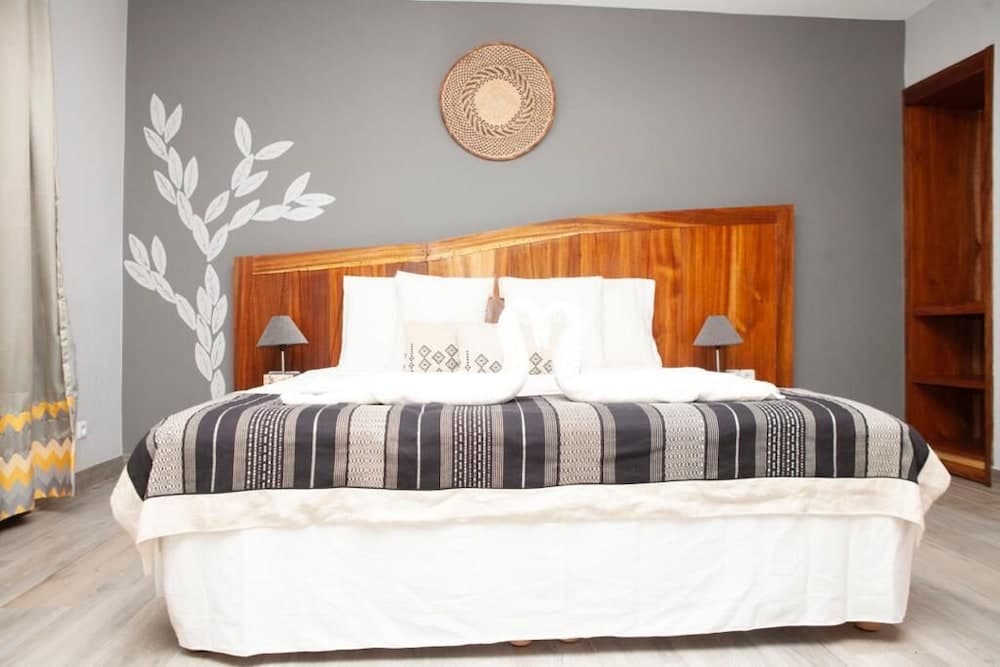 A cozy bedroom with a wooden bed adorned in patterned bedding, a woven wall hanging, and minimalist decor offers a serene retreat for travelers seeking comfort and style.