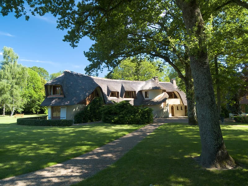 A serene countryside retreat features a charming thatched-roof cottage nestled among lush greenery, ideal for travelers seeking a peaceful escape in a picturesque rural setting.
