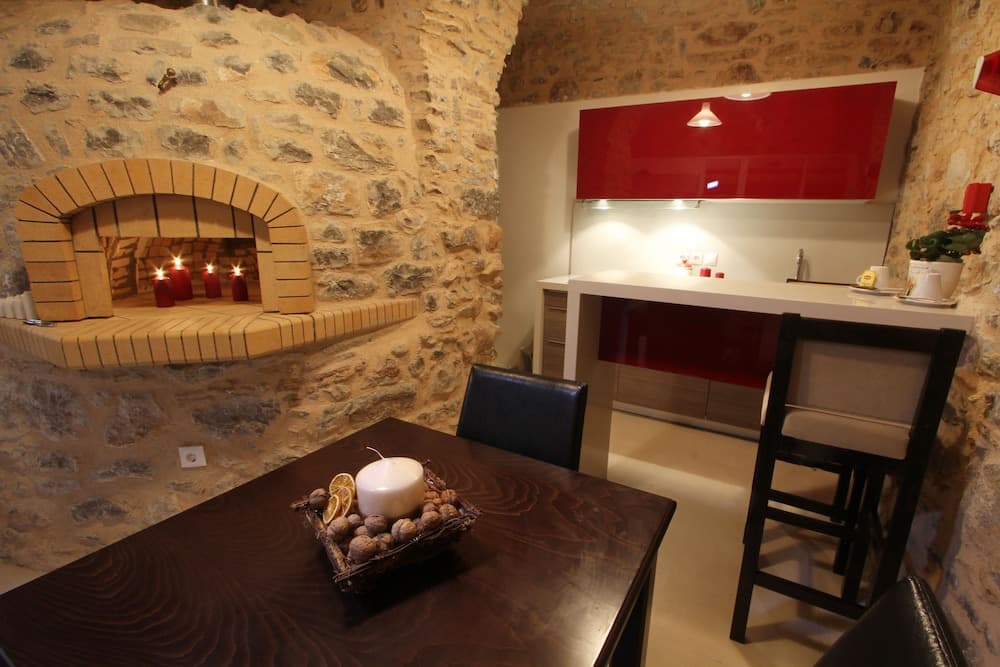 A cozy stone-walled kitchen with a rustic brick oven, modern red cabinetry, and a warmly lit dining area creates an inviting atmosphere perfect for a romantic getaway or culinary retreat.