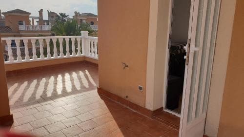A cozy balcony with white railings and terracotta tiles bathed in sunlight invites travelers to relax and enjoy the serene ambiance of a Mediterranean-style residential area.