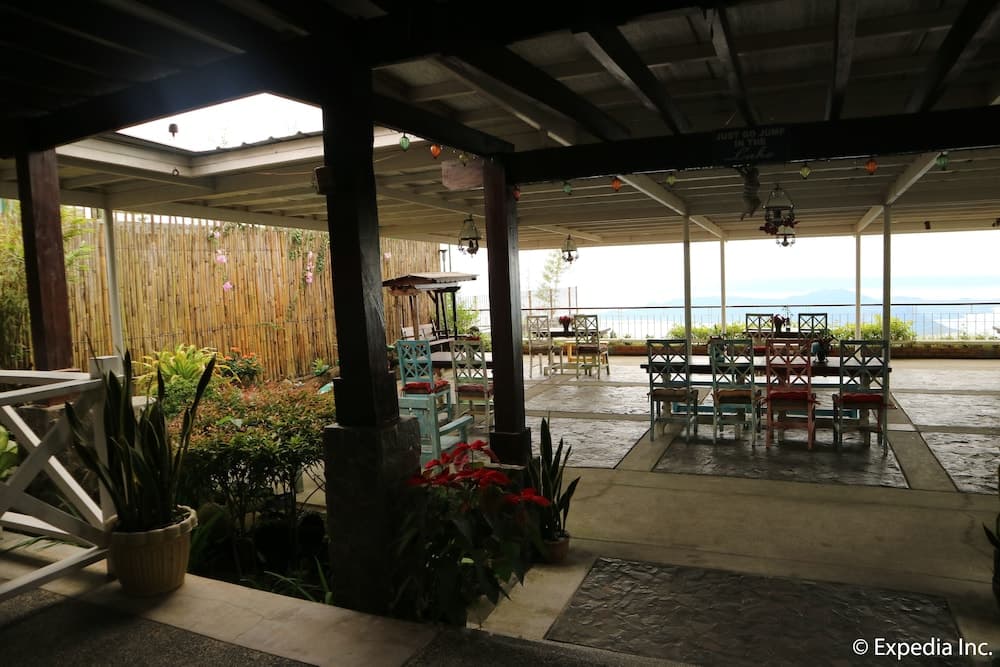 A serene lakeside patio features colorful chairs under a wooden pergola adorned with string lights, surrounded by lush greenery, ideal for tranquil retreats and scenic dining experiences.