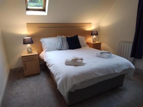A cozy bedroom with a neatly made bed, soft lighting from bedside lamps, and a window letting in natural light creates a serene atmosphere ideal for travelers seeking relaxation and comfort.
