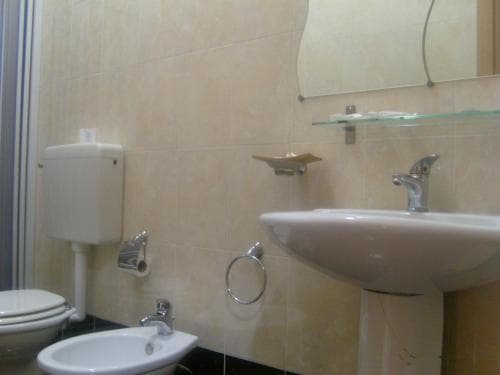 A cozy bathroom with beige tiled walls, a sink, bidet, toilet, and mirror exudes a clean and functional atmosphere, ideal for travelers seeking comfort in accommodations.