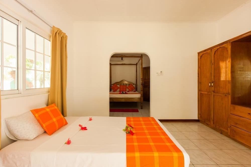 A cozy hotel room with vibrant orange accents, wooden furnishings, and floral decorations offers a serene retreat for travelers seeking comfort and relaxation.