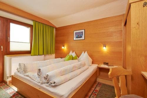 A cozy wooden cabin bedroom with warm lighting, neatly arranged bedding, and a rustic desk, ideal for a serene mountain retreat experience.