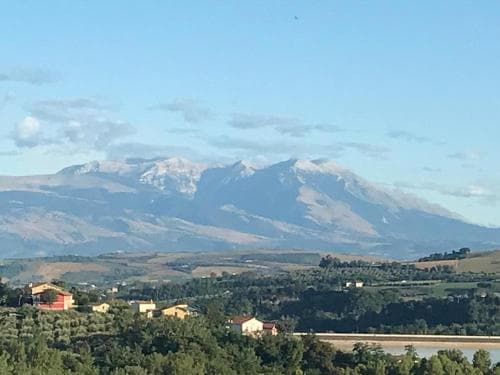 A serene countryside view featuring snow-capped mountains in the distance, quaint houses nestled among lush greenery, ideal for tranquil retreats and nature photography.