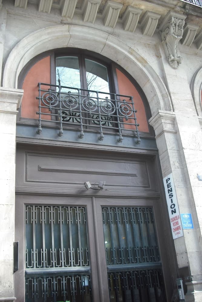 A historic building entrance featuring an arched window with ornate ironwork and a "PENSION" sign, ideal for travelers seeking budget-friendly accommodations in a charming urban setting.