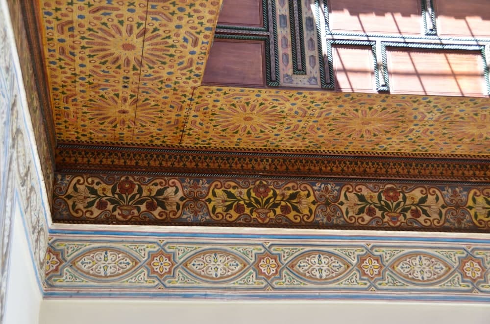 A vibrant, intricately painted ceiling adorned with floral and geometric patterns bathes a historic indoor space in warm sunlight, ideal for cultural heritage tourism and photography enthusiasts.