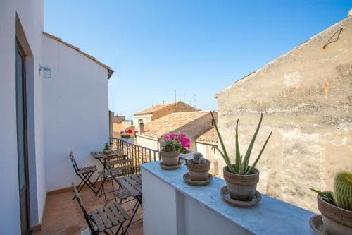 A serene rooftop terrace adorned with potted plants and chairs overlooks charming old buildings under a clear blue sky, ideal for travelers seeking a peaceful retreat in a historic setting.
